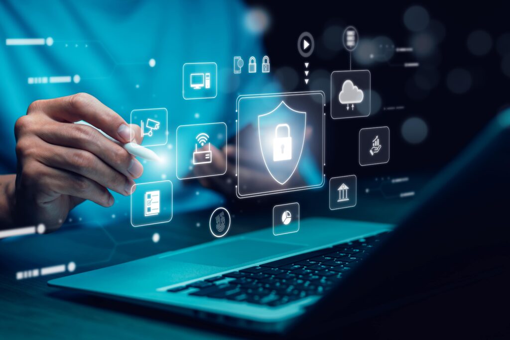 A person uses a stylus to interact with a digital screen displaying security icons like a lock and cloud above a laptop