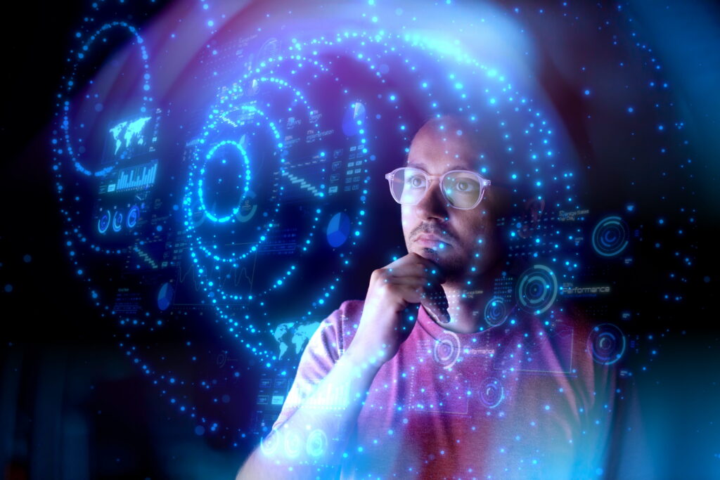An individual wearing glasses looks thoughtfully ahead while interacting with a futuristic digital interface, surrounded by glowing blue data visualizations, charts, and circular HUD elements against a dark background.